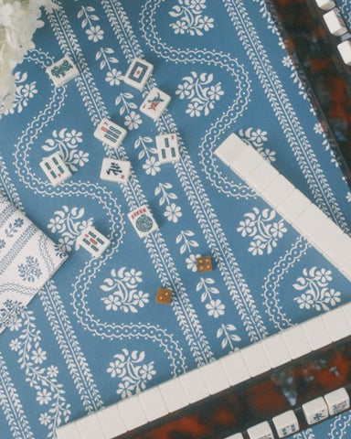 A blue and white patterned Mahjong table with tiles arranged in rows, alongside a scalloped tortoiseshell mahjong racks.