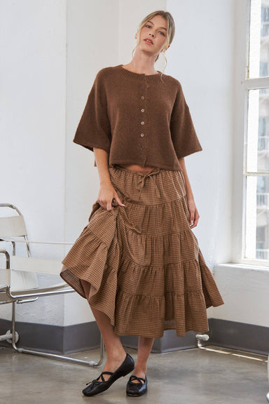 Woman wearing a brown top and ruffled skirt in a room with a window.