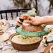 Person using a decorative pheasant-shaped serving tool to serve food on a table with glasses and plates.