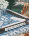 A mahjong set displayed on a blue and white patterned tablecloth in an outdoor garden setting with wooden chairs and warm string lights in the background.