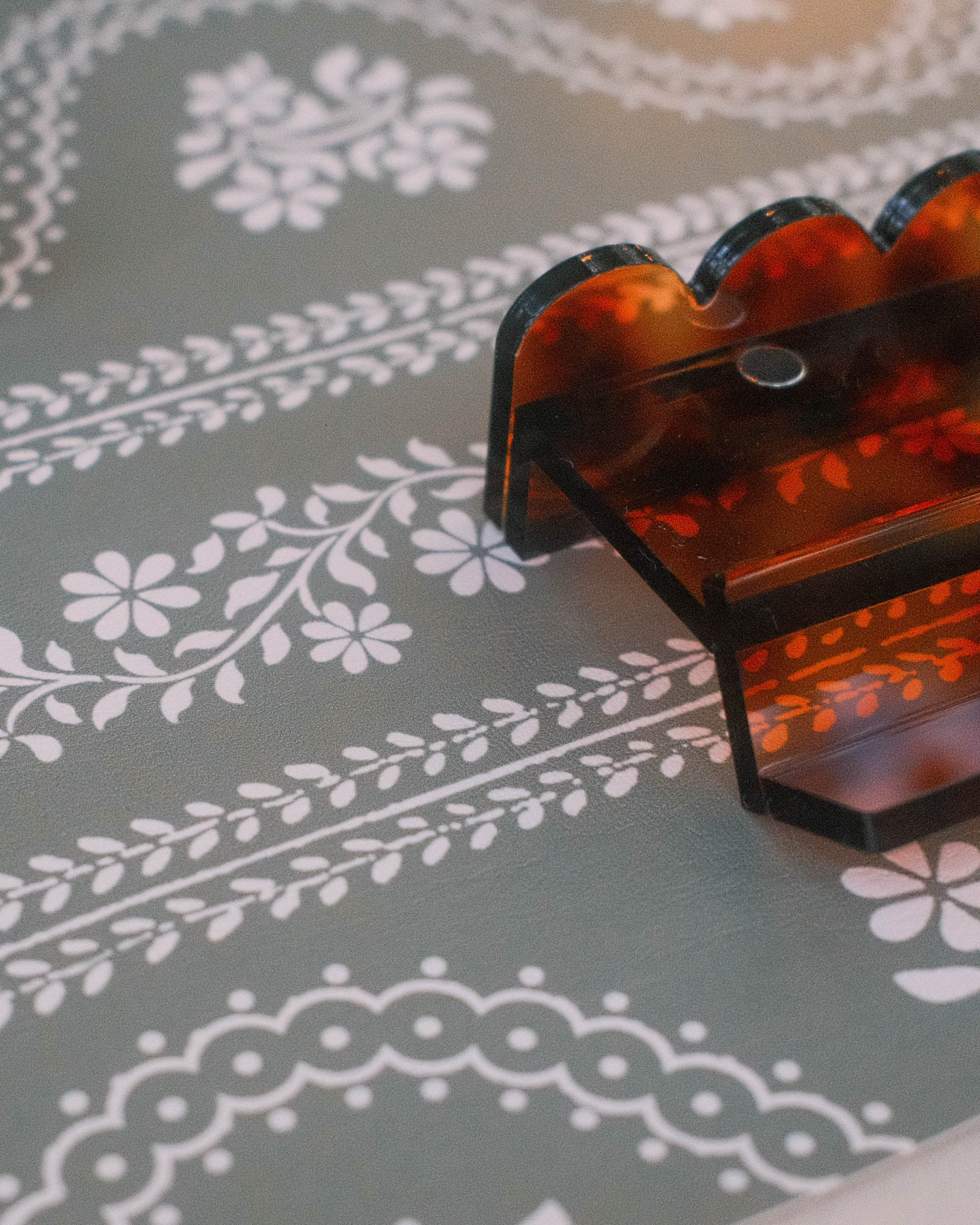 A close-up of a scalloped tortoiseshell mahjong rack on a green floral serpentine leatherette mahjong mat.