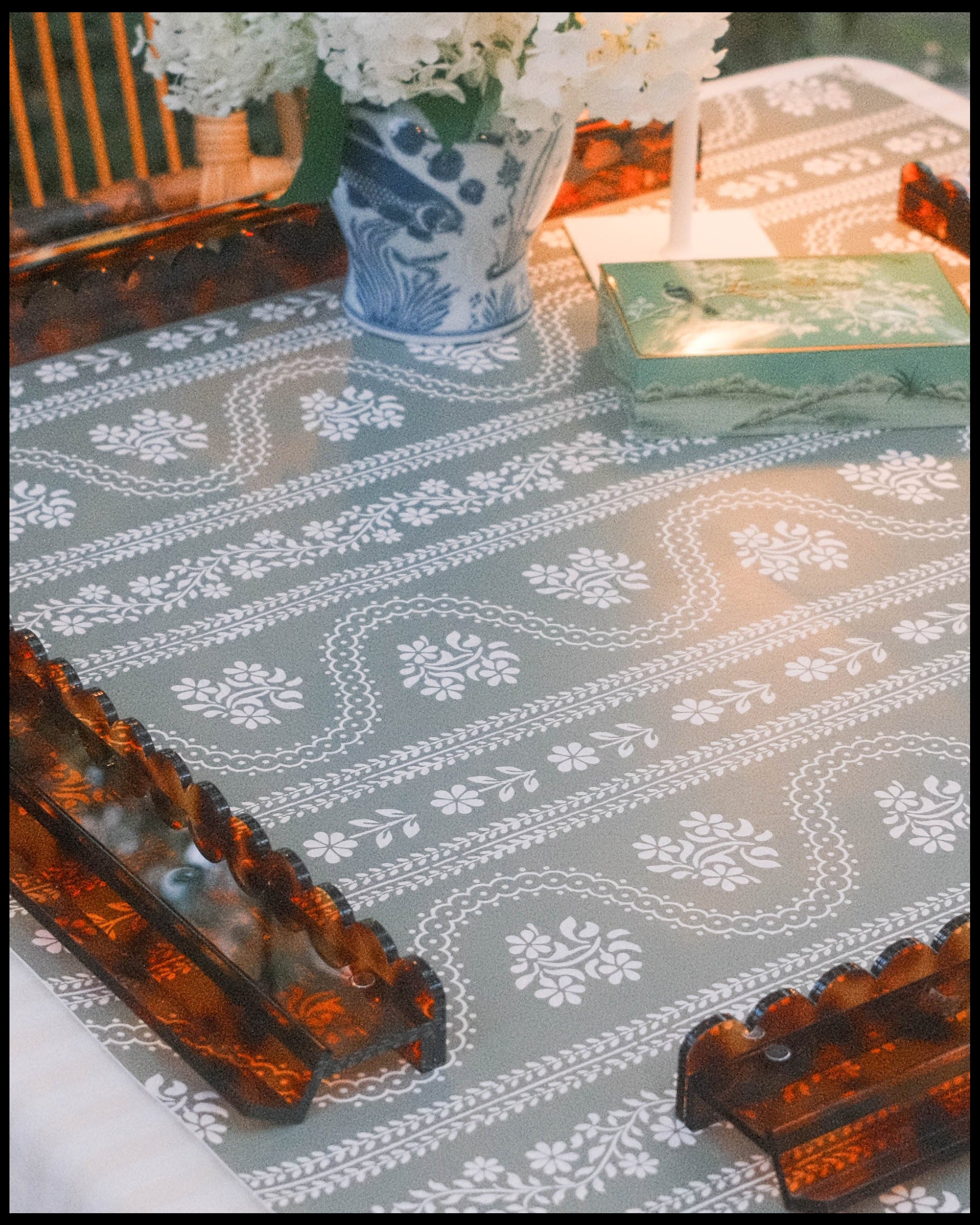 A styled mahjong setting featuring four scalloped tortoiseshell mahjong racks on a green serpentine floral leatherette mahjong mat. 
