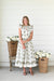 Ivory midi dress with olive green floral block print, flutter sleeves, a keyhole neckline, a smocked waist, and a flowing tiered skirt.