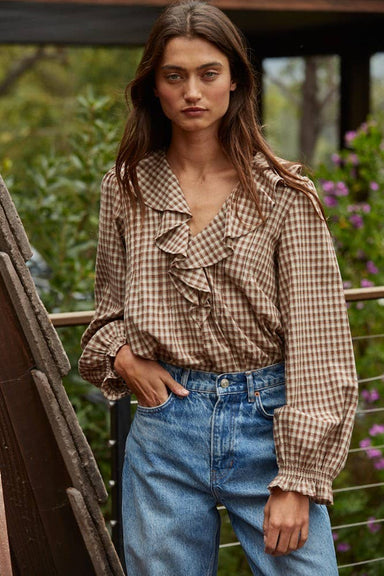 Woman wearing a plaid shirt and blue jeans standing outdoors with greenery in the background