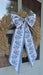 Natural wheat wreath adorned with an oversized blue and white floral bow, styled on a glass door for a warm fall entrance.
